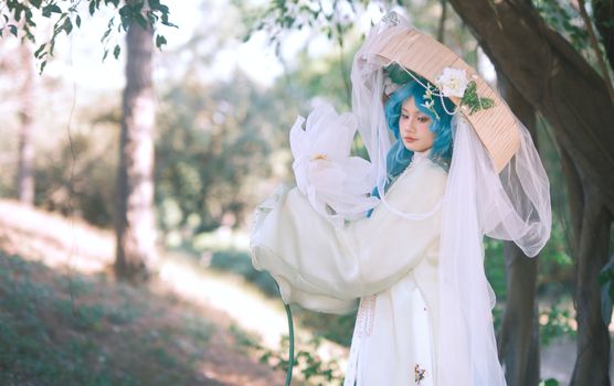 Cosplayer in elaborate costume with blue hair and floral accents set in a serene outdoor environment.