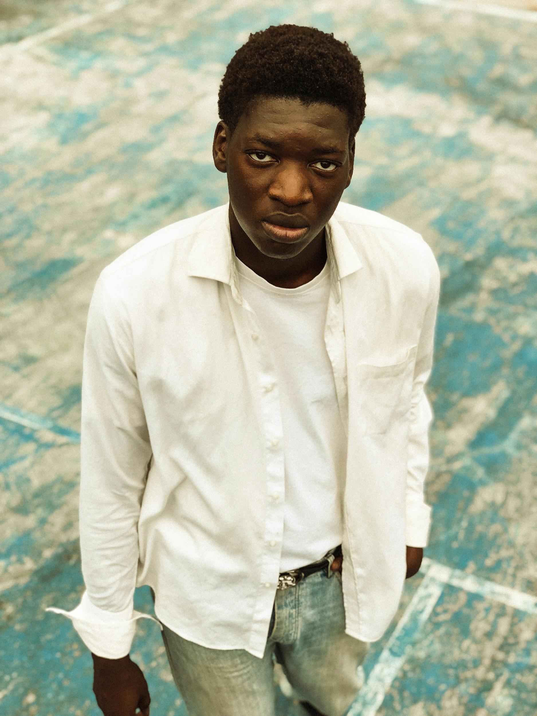 Man standing on outdoor sports court, wearing white shirt and jeans, looking up.