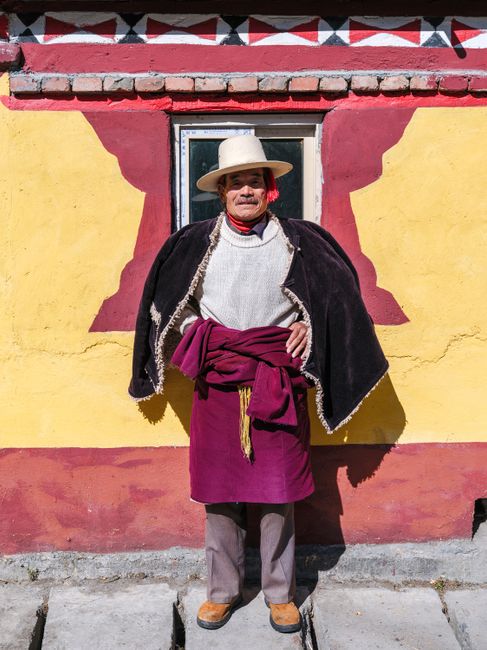 Elderly man in traditional Peruvian attire by a colorful wall.