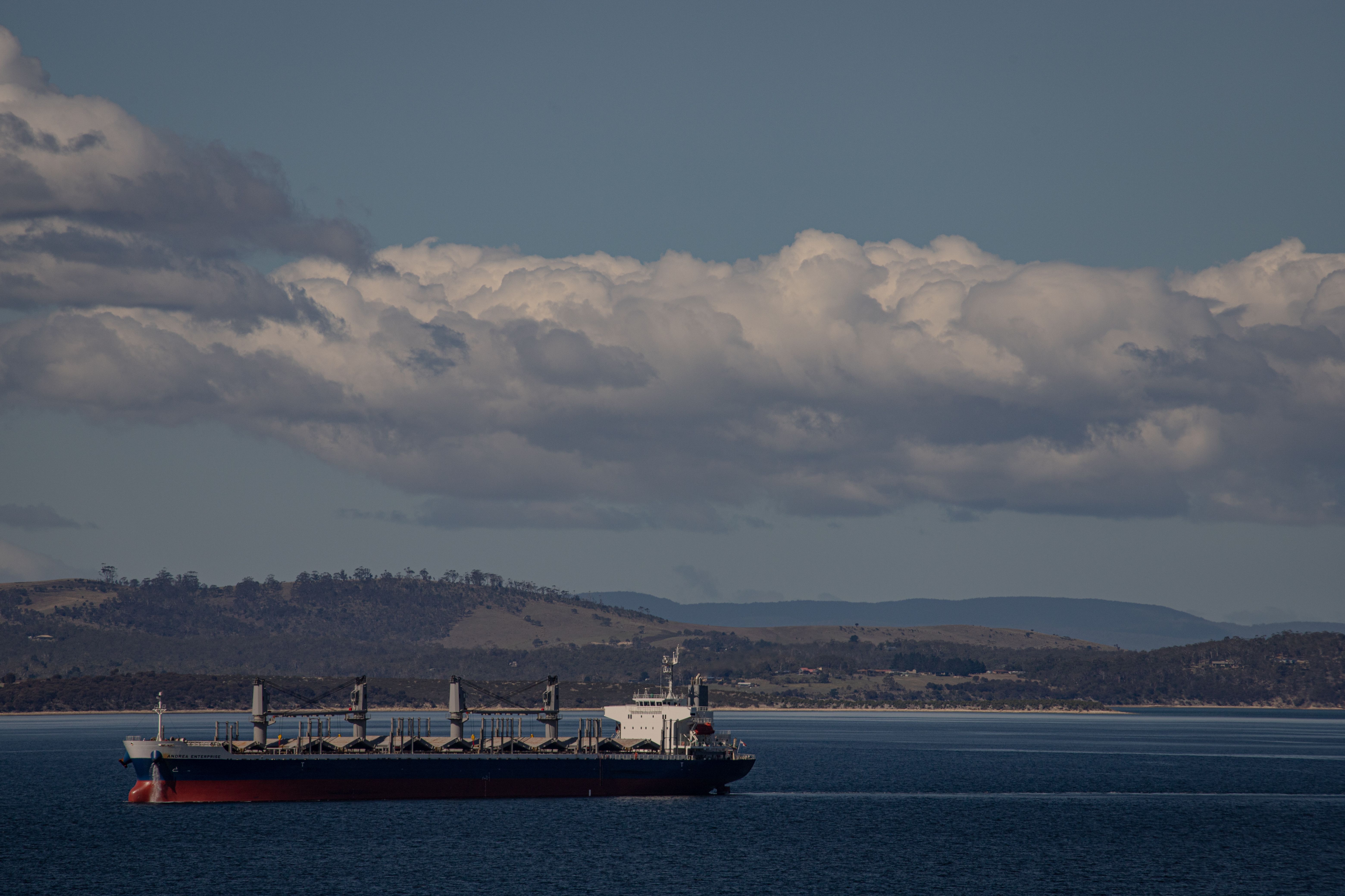 A cargo ship sails on the river with a scenic backdrop in Hobart, Tasmania under cloudy skies.