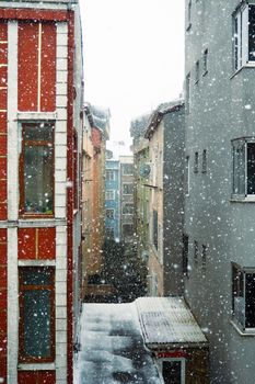 A vibrant winter scene with snow falling between colorful city buildings, creating a picturesque urban winter view.