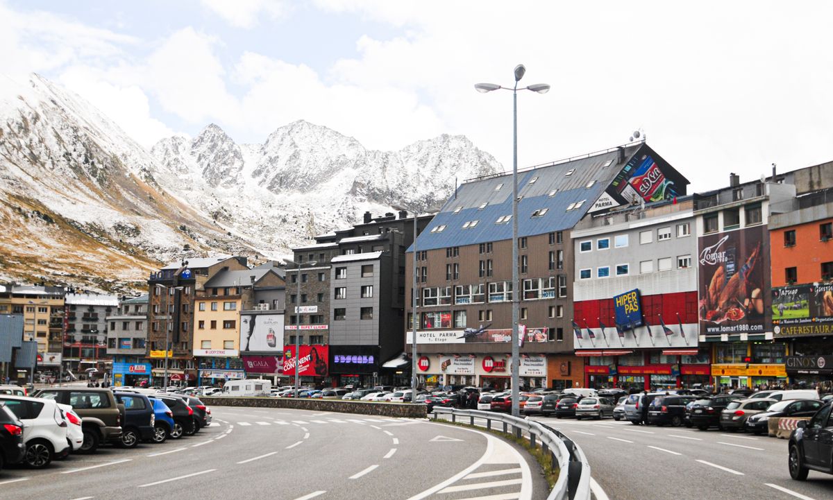 Bulevard comercial dintr-un oraș andorran, cu magazine și reclame sub piscuri înzăpezite