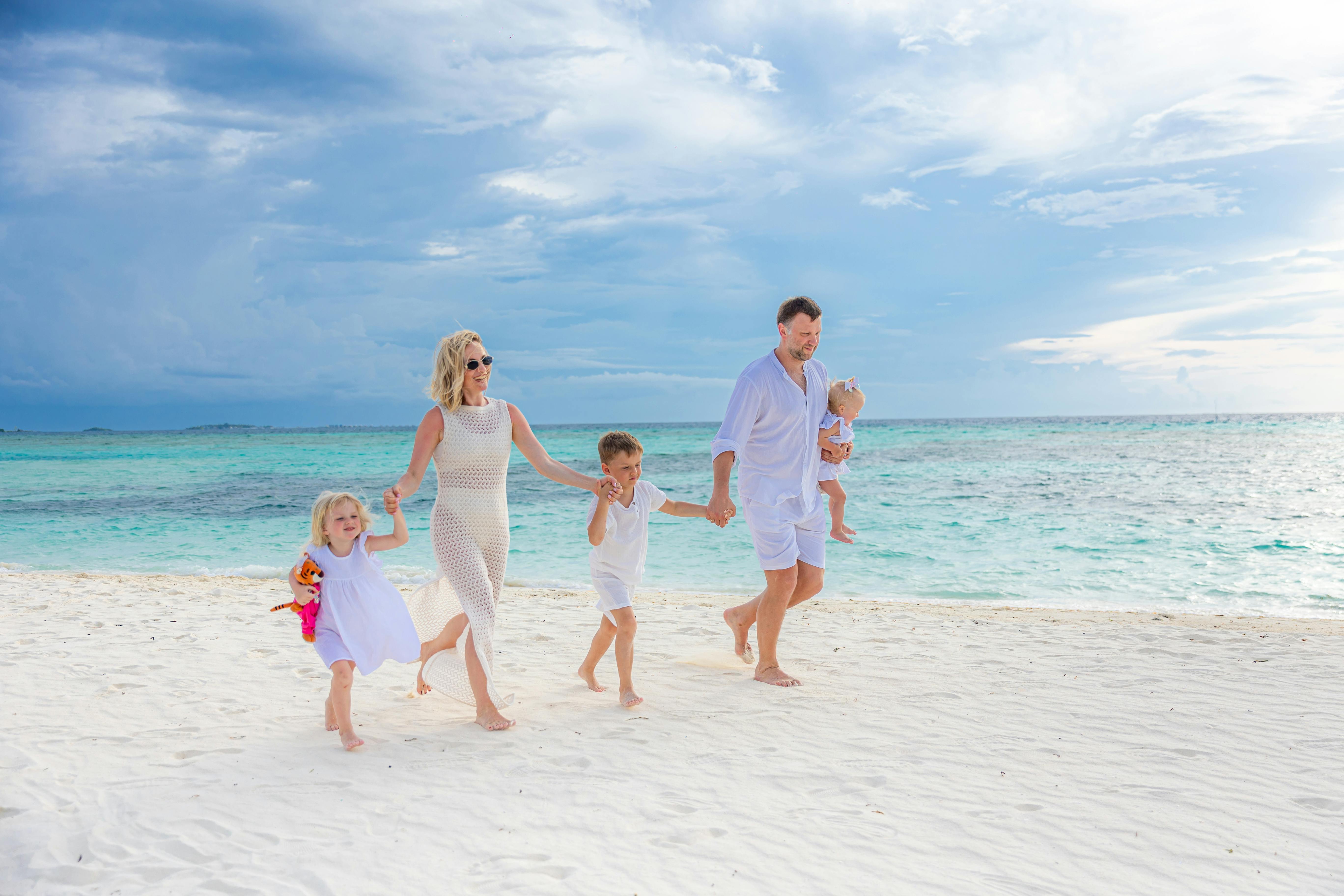Family enjoying a walk on a pristine beach with turquoise waters, captured in a light-hearted moment. - Photo by Gabdu Jomart on Pexels