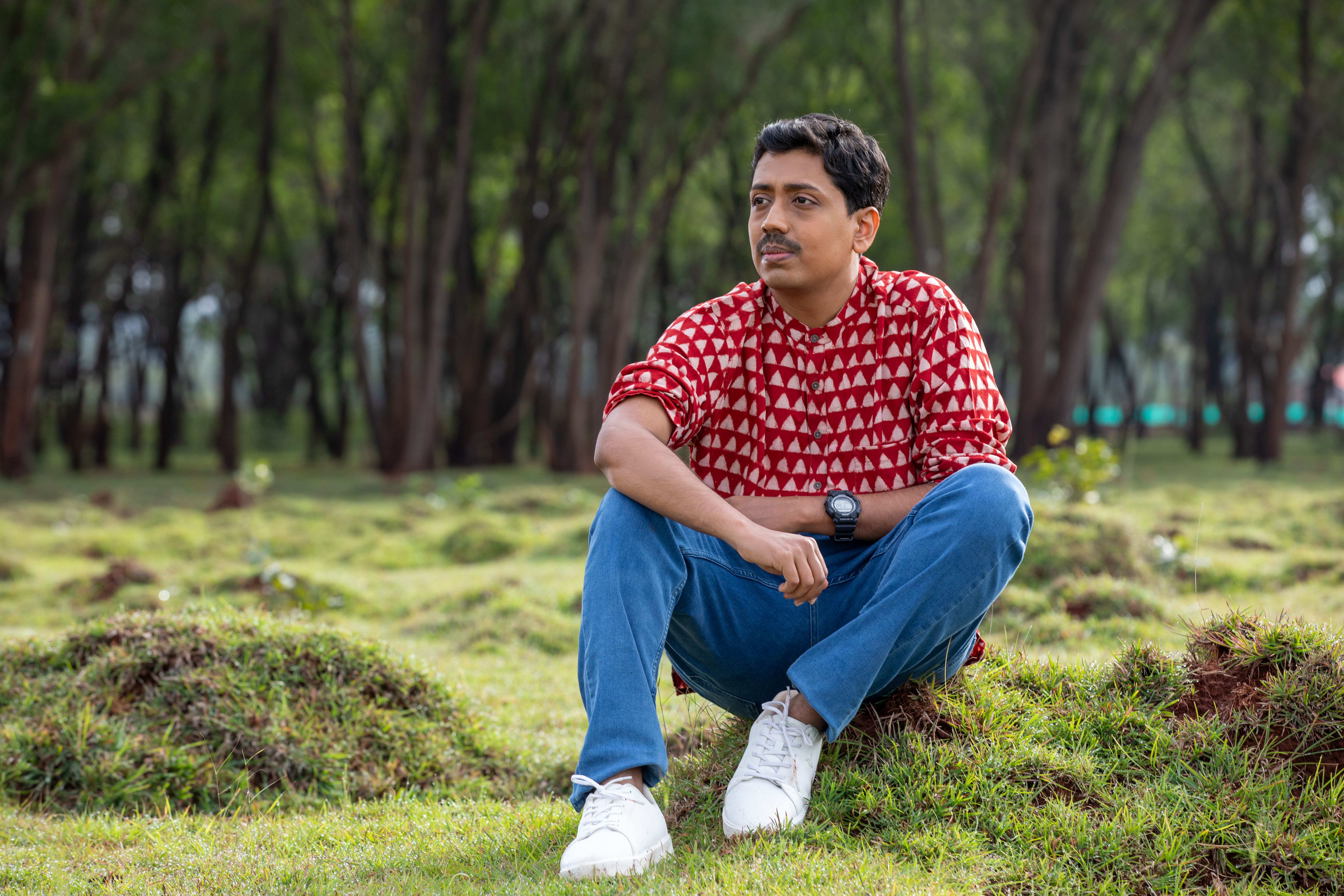 A man in casual attire sits outdoors in a grassy area, evoking a relaxed vibe.