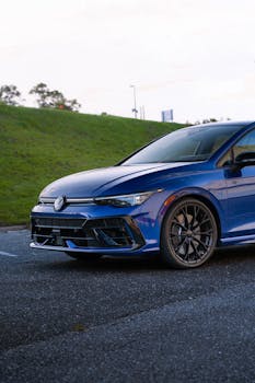 A sleek blue sports car parked on the roadside with a vibrant green hill backdrop.