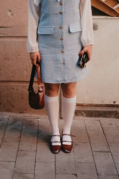 Stylish woman in vintage outfit with accessories stands on sidewalk.