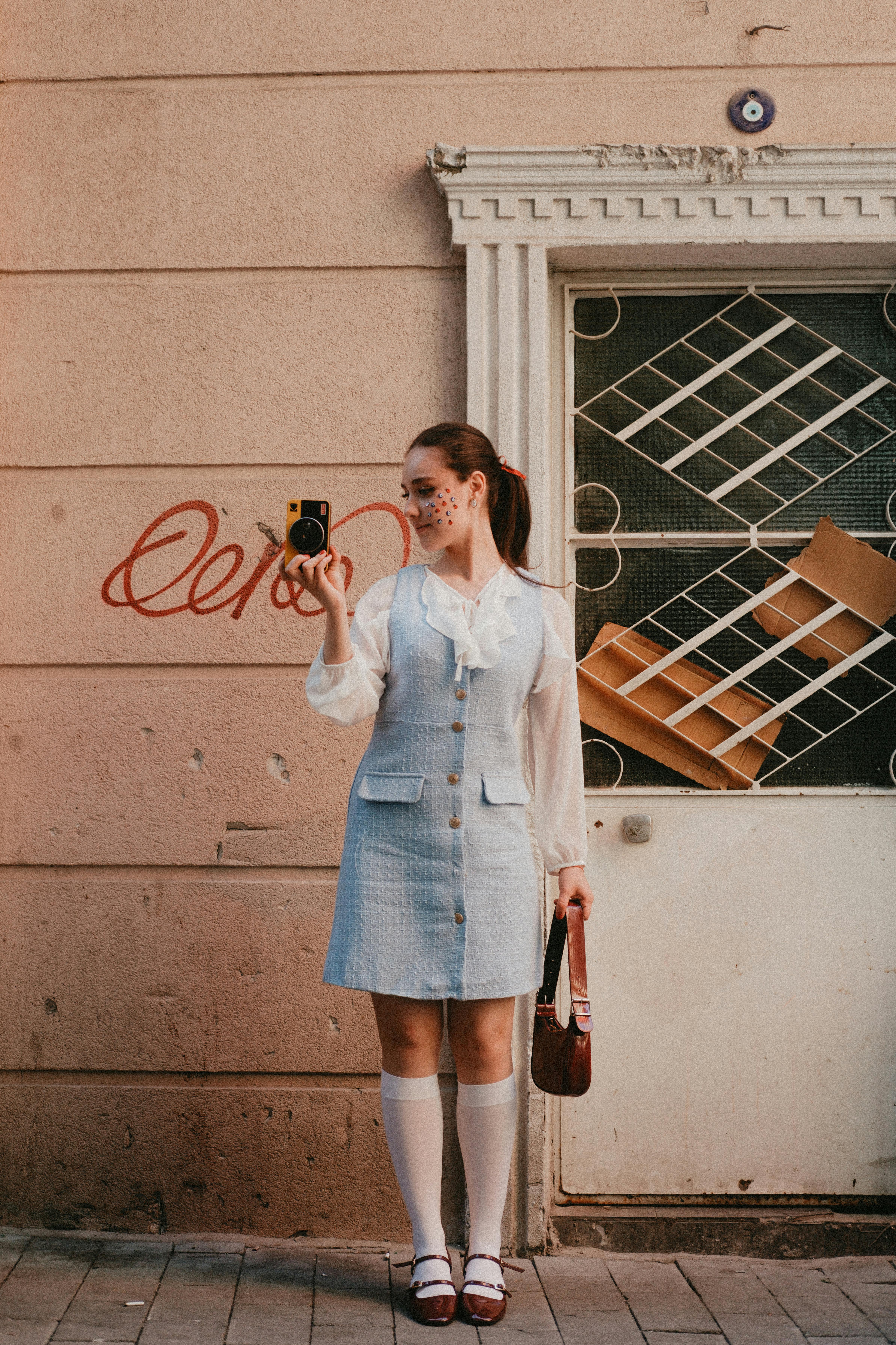 Woman in stylish outfit poses with vintage camera against urban backdrop. Retro vibes.