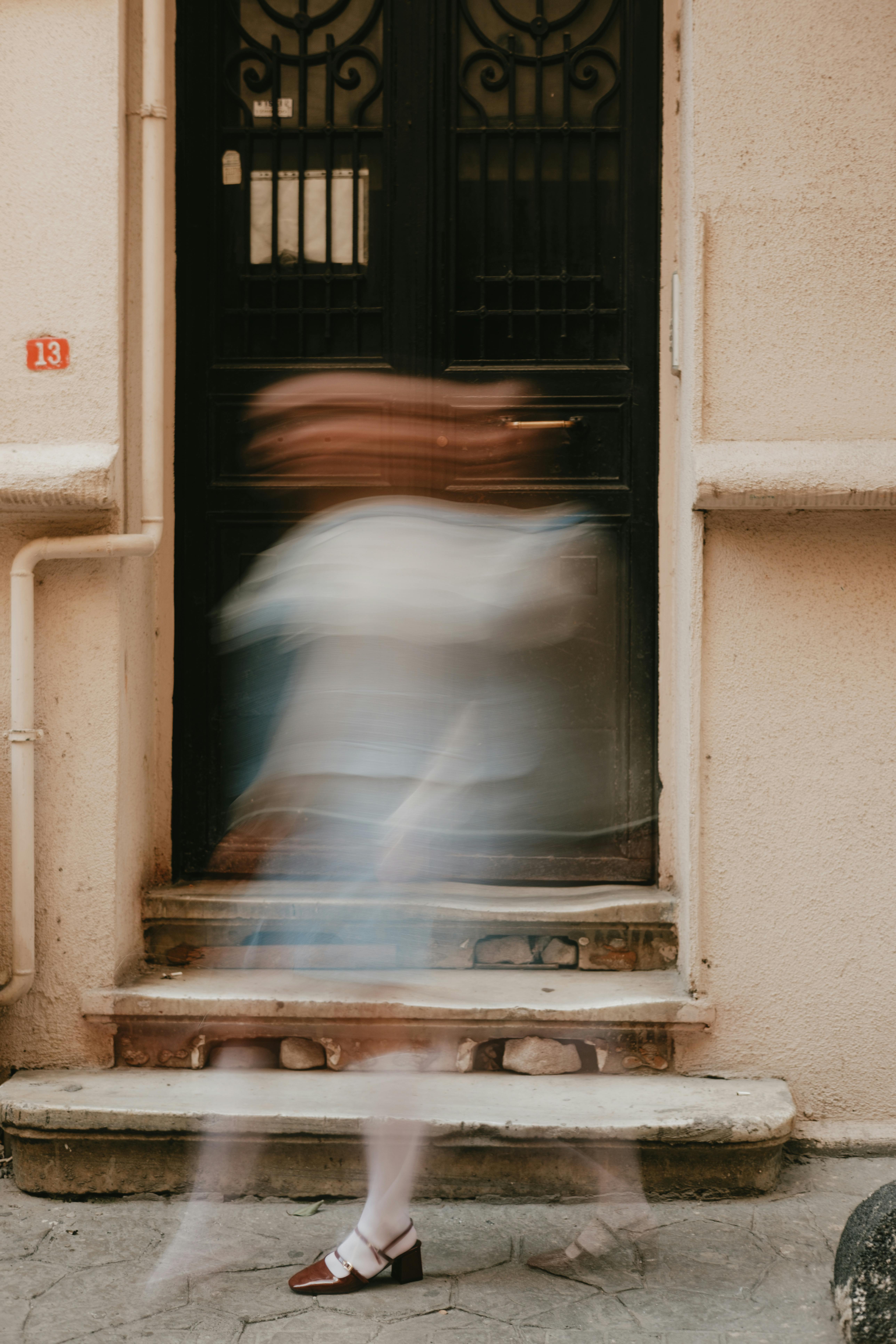 Abstract image of a person in motion blur walking past a vintage door in a city setting.