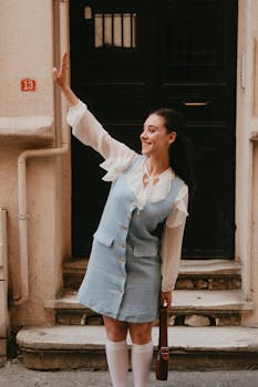 Smiling woman in vintage outfit waves at doorway, evoking nostalgia.