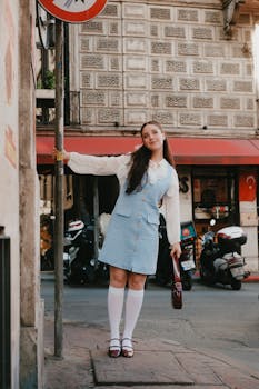 Chic young woman in urban setting, leaning on signpost in fashionable attire.