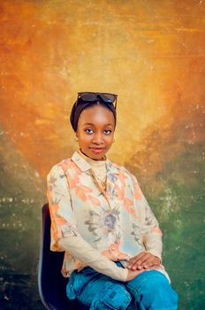 Stylish young woman sits confidently in a floral shirt, over a warm-toned background.