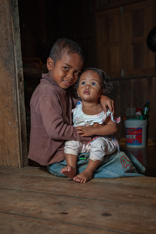 Free A young boy lovingly holds his baby sibling inside a wooden home. Stock Photo