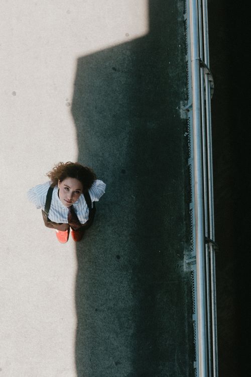 Free Aerial view of a woman standing on concrete, partially lit by shadow, outdoors. Stock Photo