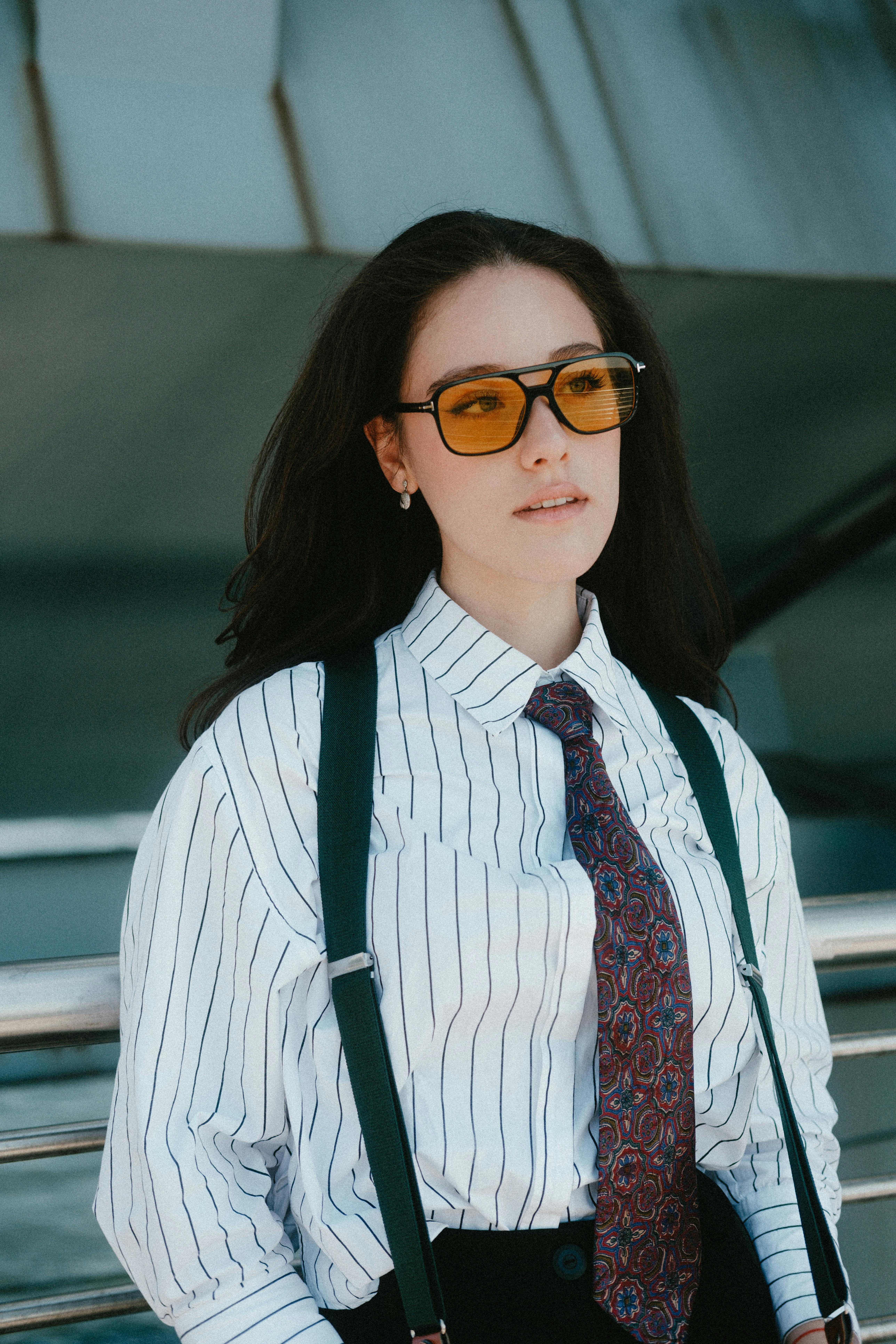 Fashionable woman wearing sunglasses and striped shirt posing confidently outdoors.