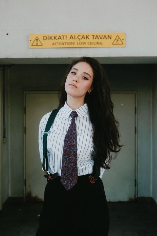 Free Confident young woman in a striped shirt and tie under a low ceiling sign. Stock Photo