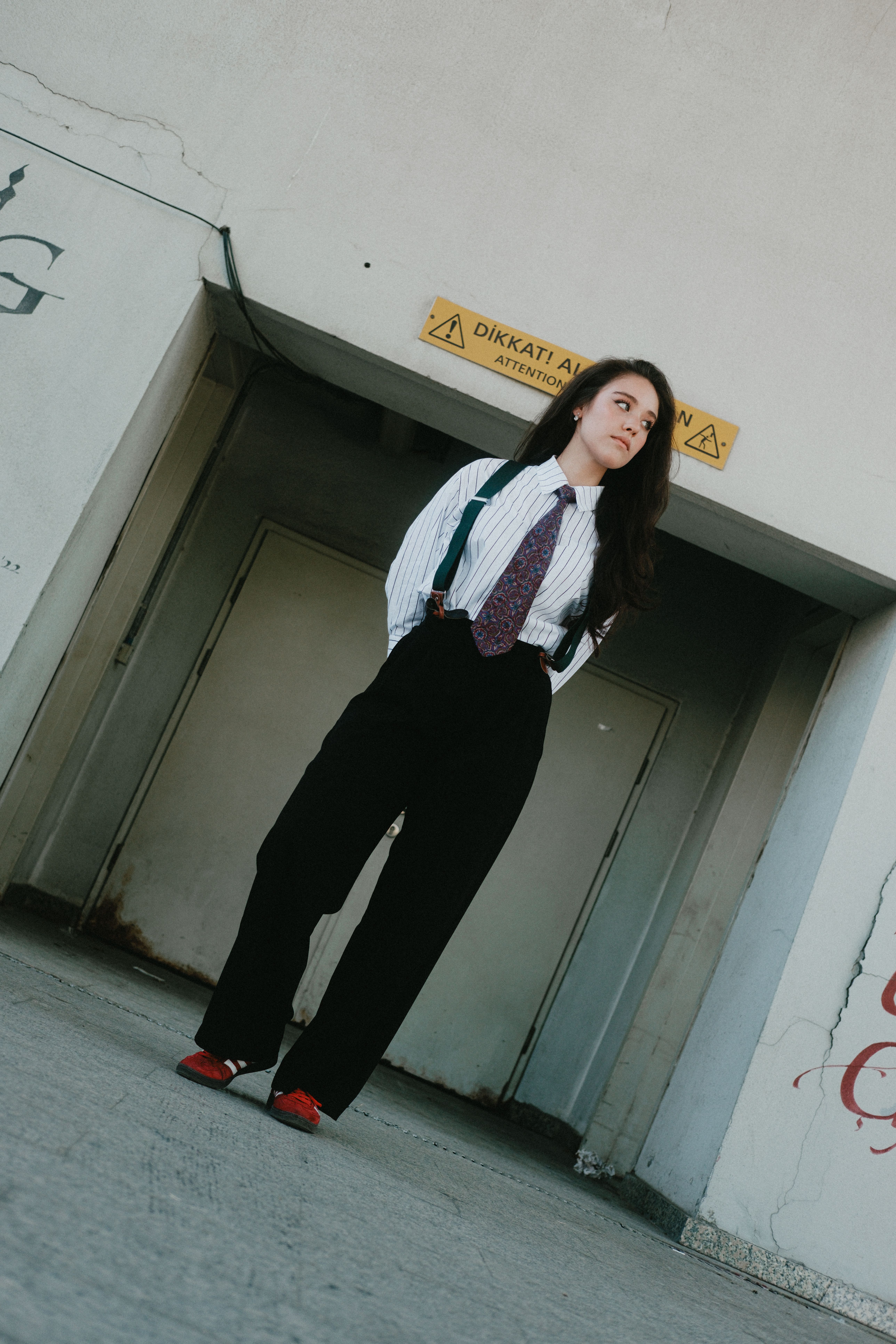 Stylish woman in suit with suspenders poses confidently outside an urban building.