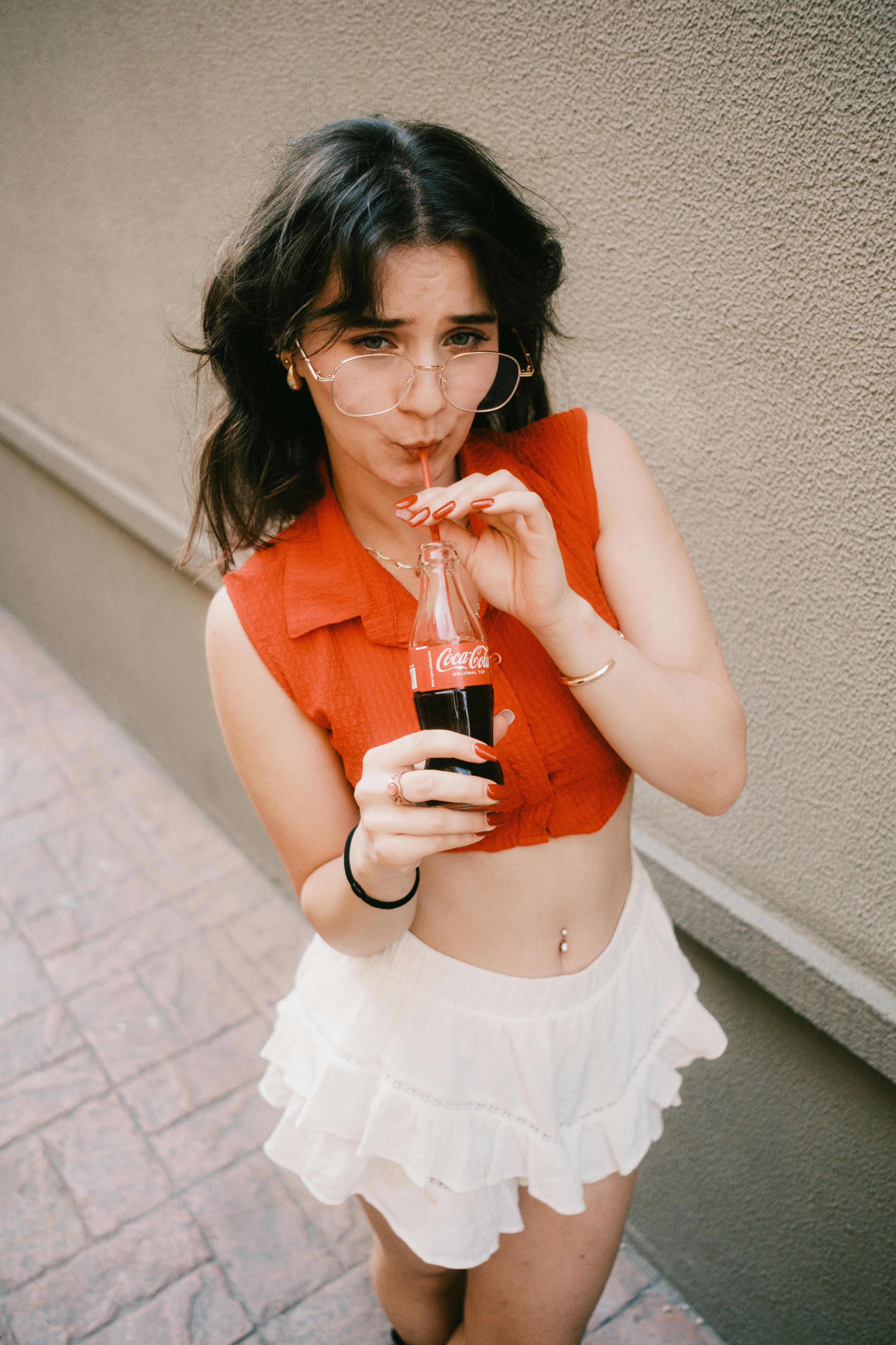 Stylish young woman with sunglasses sipping Coca-Cola outdoors, exuding a relaxed summertime vibe.
