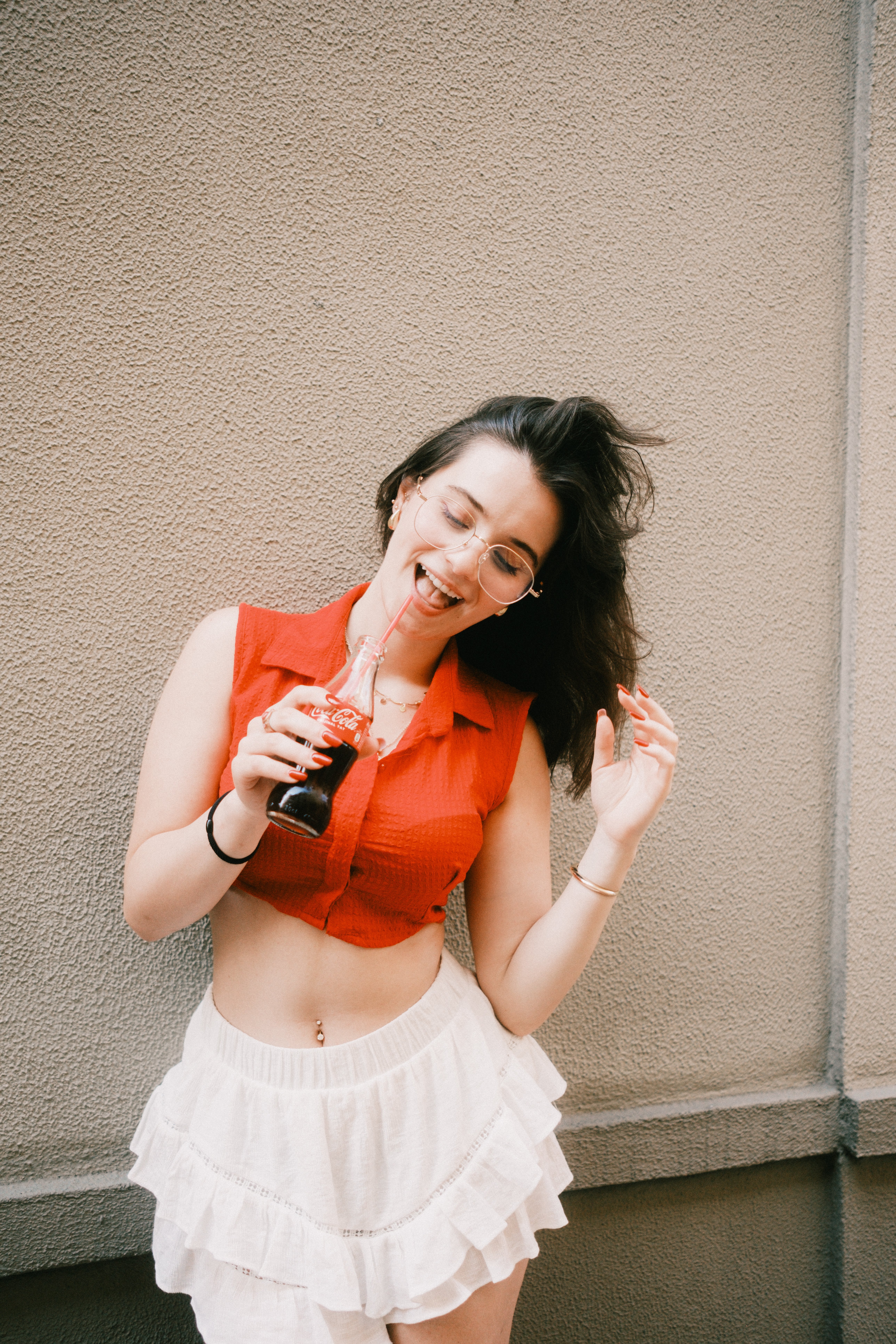 Cheerful woman in red top and white skirt enjoying a soft drink on a sunny day.