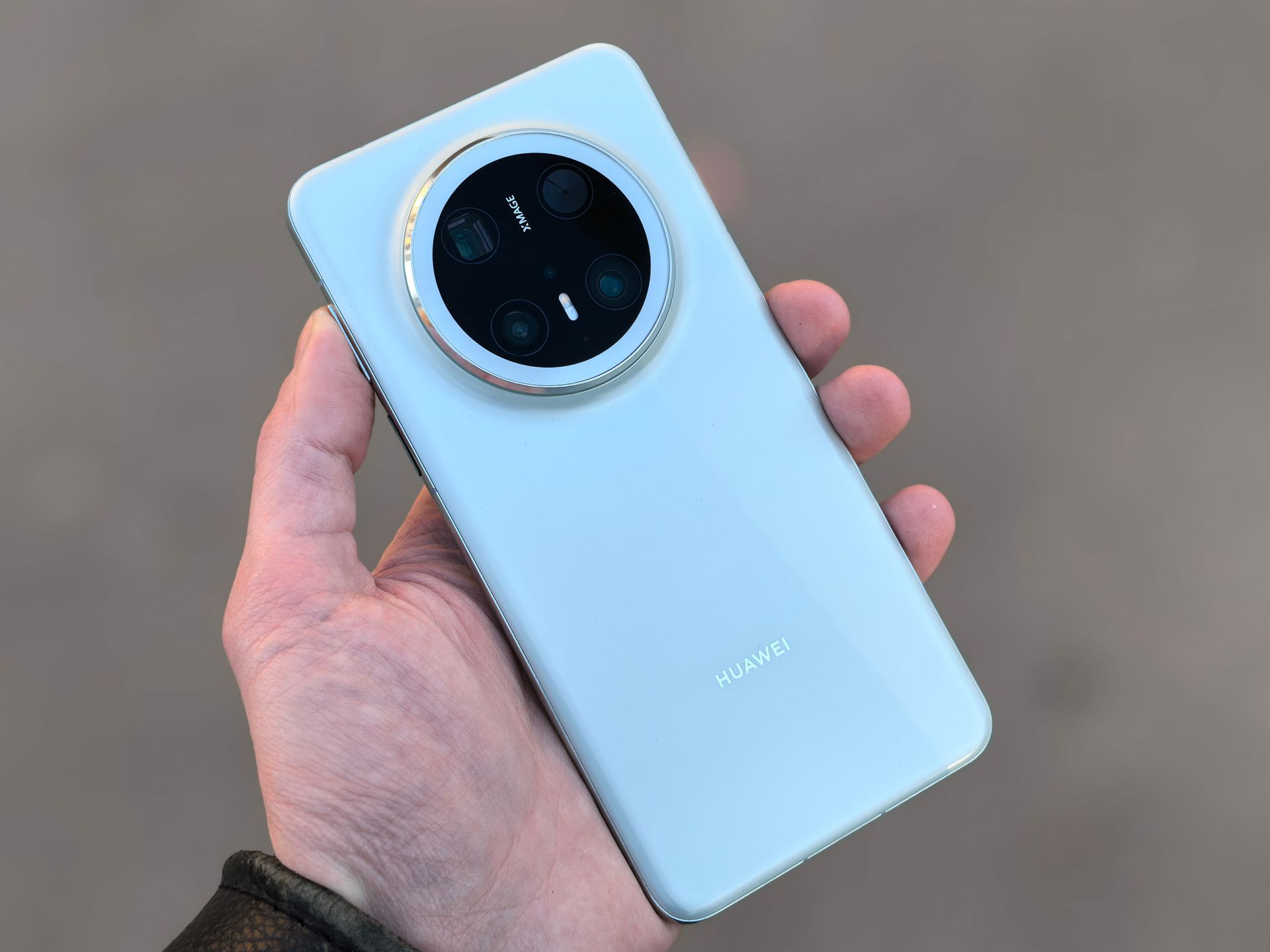 Close-up of a hand holding a sleek smartphone featuring a quad camera setup and shiny finish.