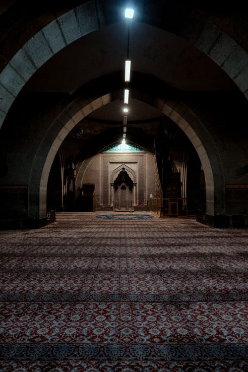 Free Elegant mosque interior showcasing grand arches and rich patterned carpet, basked in dim light. Stock Photo