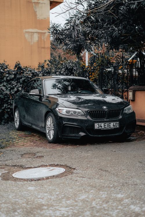 Free A sleek black sedan parked outdoors near a hedge on a cloudy day, showcasing details of the urban environment. Stock Photo