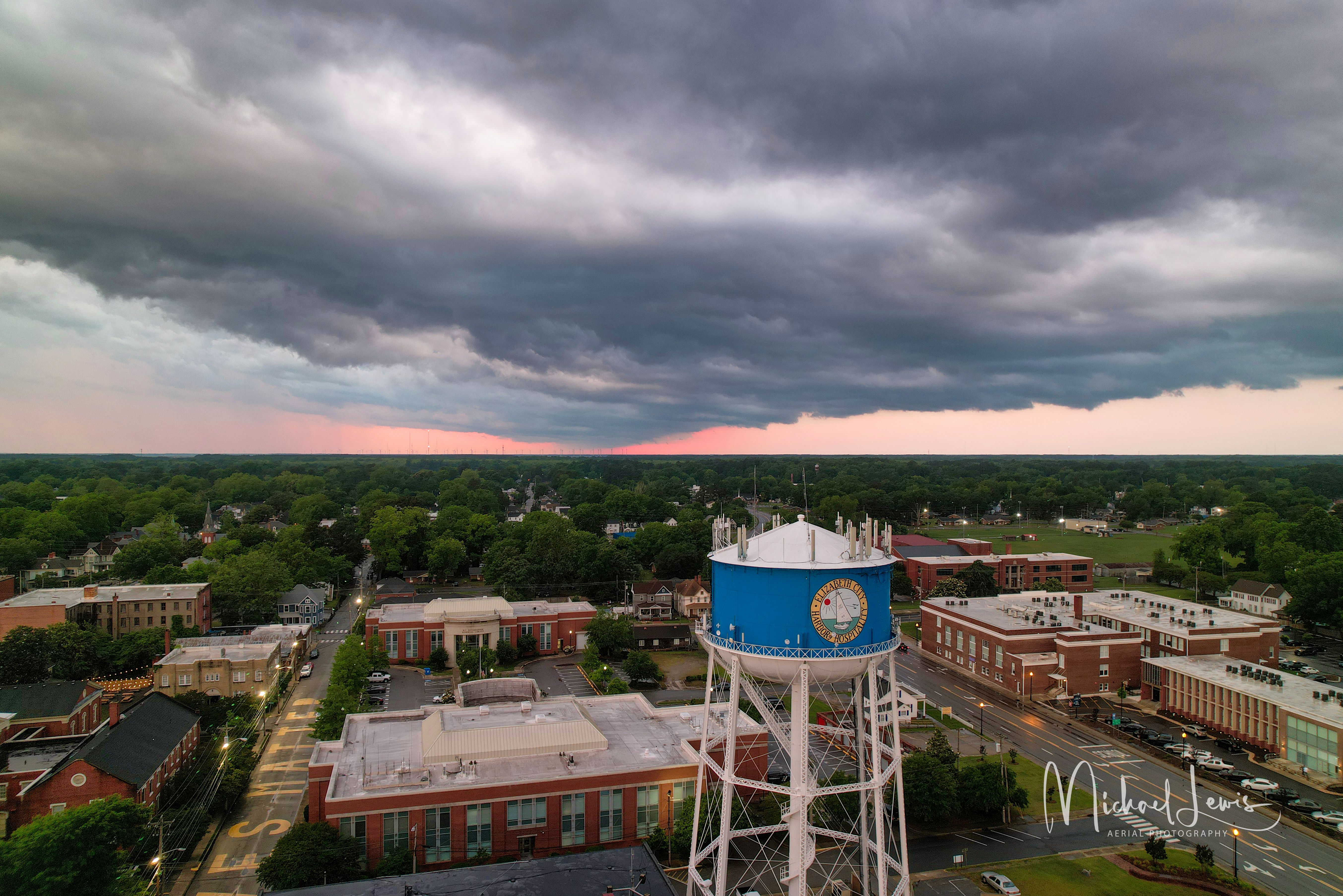 Dramatic aerial shot of a town featuring a blue water tower under moody sunset skies.