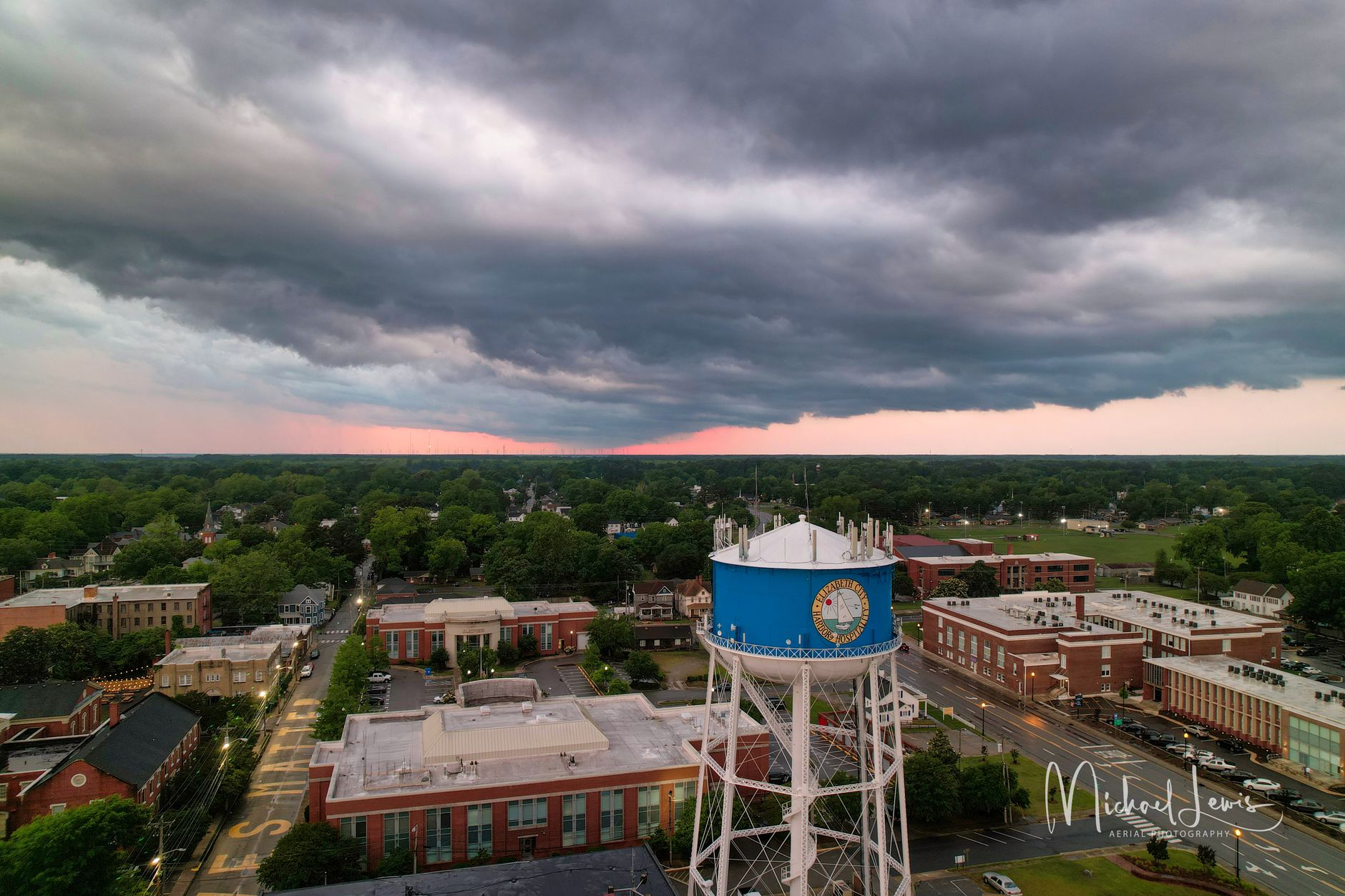 Dramatic aerial shot of a town featuring a blue water tower under moody sunset skies.