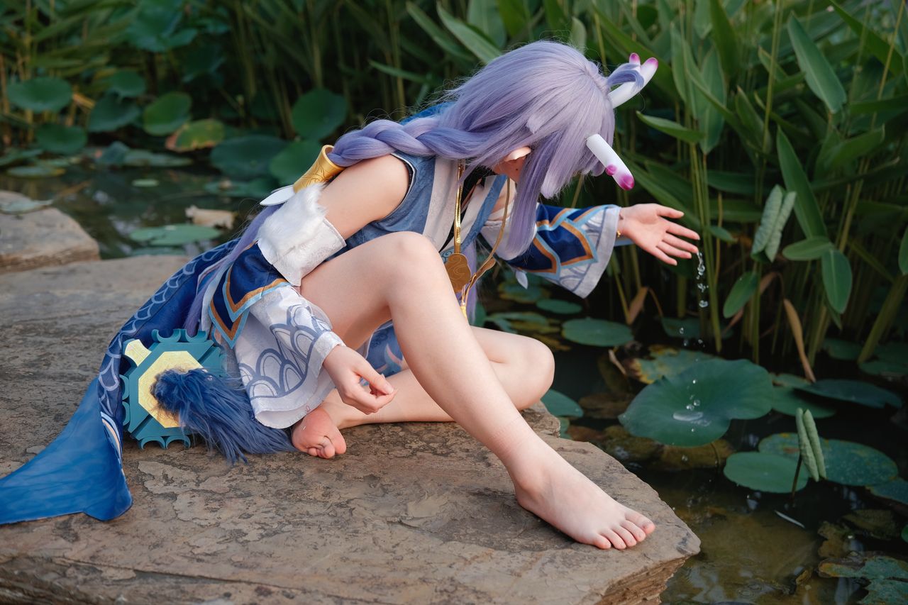 a person in elaborate cosplay costume sitting by a serene pond touchin