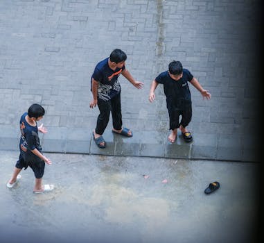 Three kids enjoying the rain, creating joyful childhood memories on a wet urban street.