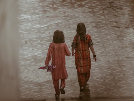 Two children playing in rain wearing colorful clothes, capturing authentic monsoon joy.