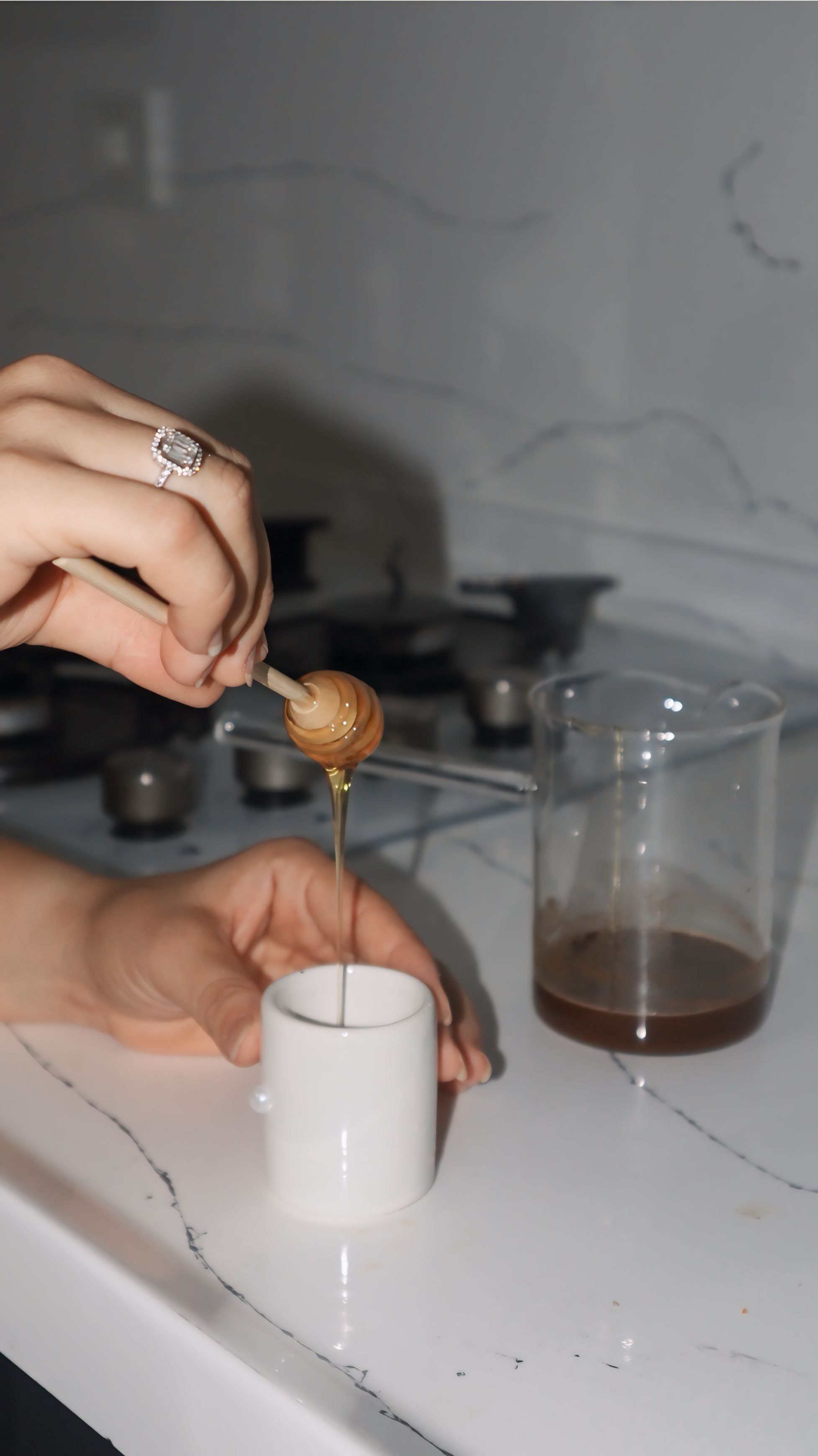 Hand pouring golden honey into a small white cup in a sleek kitchen setting.