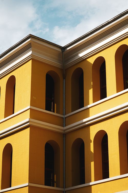 Free Elegant yellow building corner with arches in sunlight against a blue sky, showcasing vibrant architecture. Stock Photo