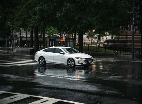A sleek white car drives through wet streets of Washington DC after a rain shower.