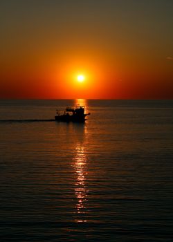 Fishing boat silhouette against a vibrant sunset on a calm ocean, creating a peaceful evening scene.