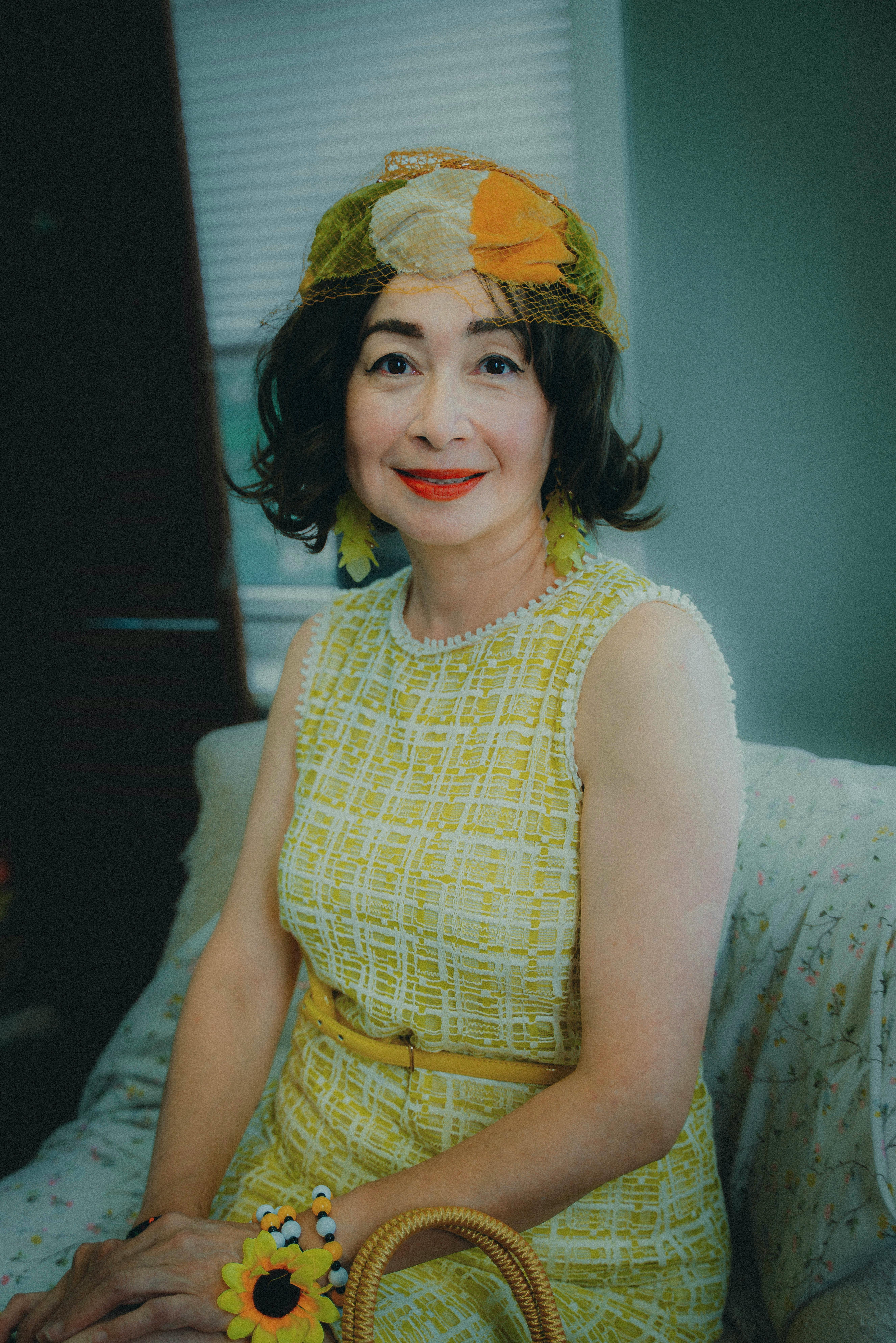Stylishly dressed woman in vintage yellow dress and hat, seated indoors.