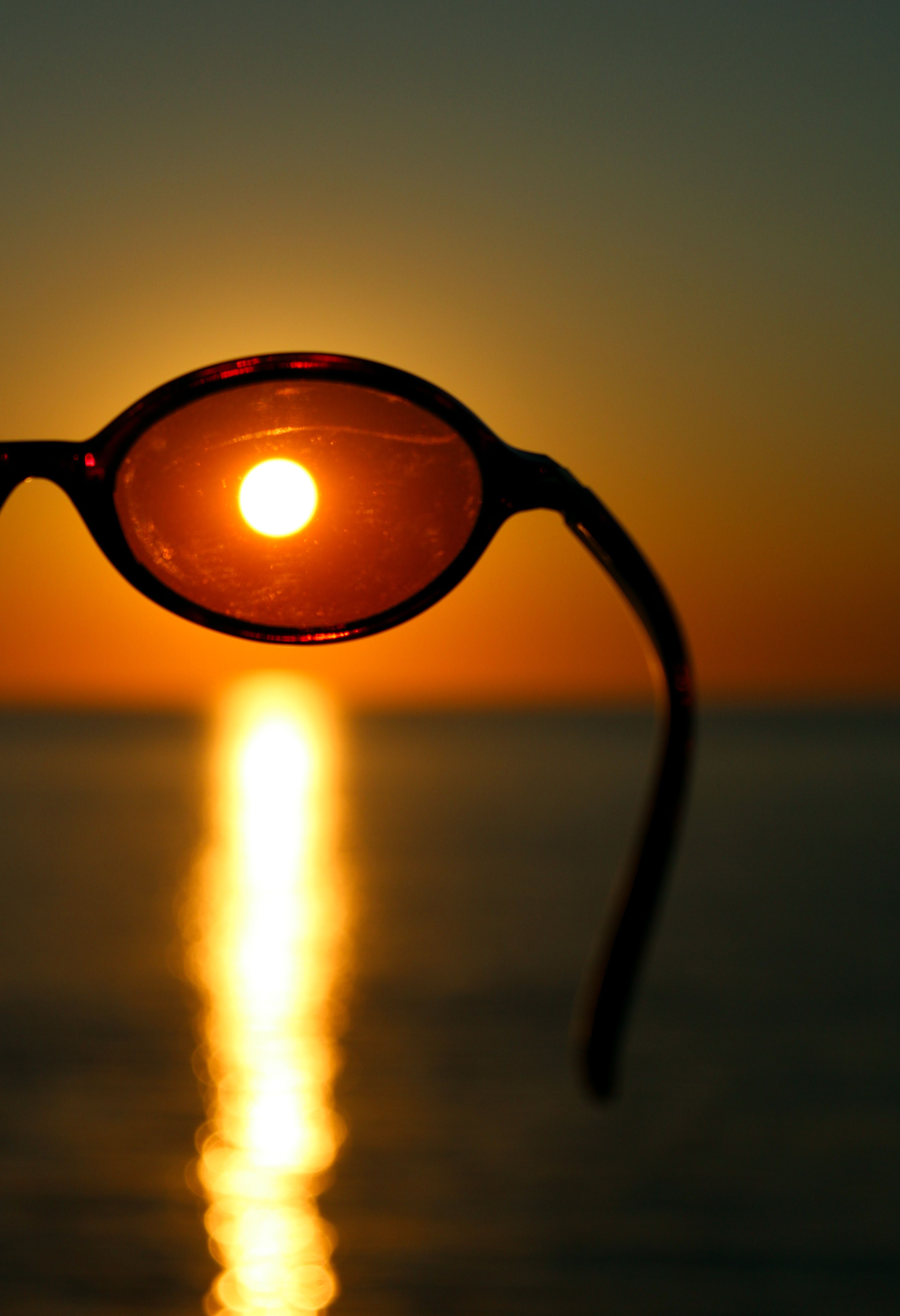 Silhouette of sunglasses framing the sun during a vibrant ocean sunset.
