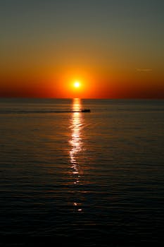 Calm ocean scene with a vibrant sunset and a distant silhouette of a boat.