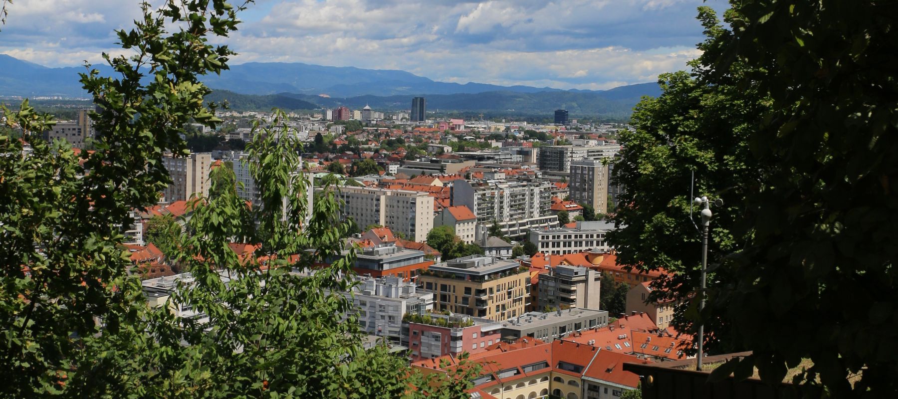A vibrant cityscape of Ljubljana, Slovenia, framed by lush greenery and a clear sky.
