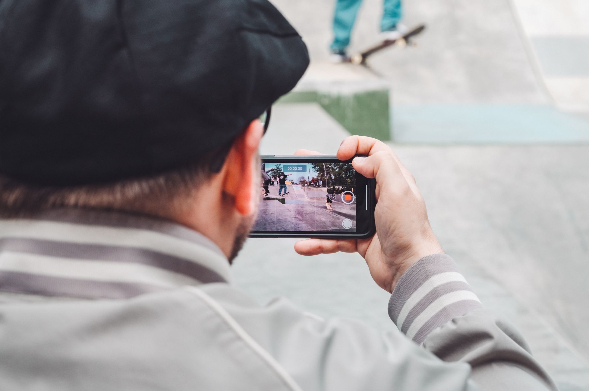 Person filming skateboarding action at a skatepark using a smartphone. Urban lifestyle and technology concept.