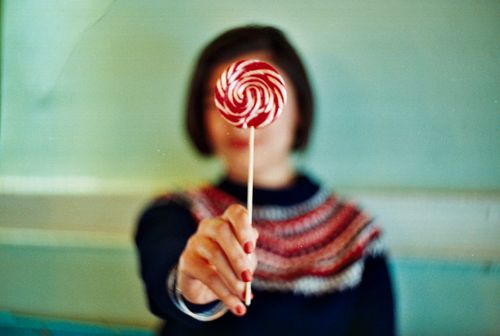 Free Blurred woman holding a vibrant red and white lollipop with focus on the candy. Stock Photo