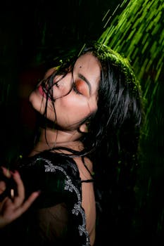 A woman with closed eyes relishes the rain at night, captured in moody lighting.
