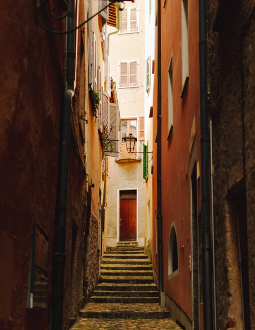 Free Explore the rustic charm of a narrow European alley with bright walls and cobblestone path. Stock Photo