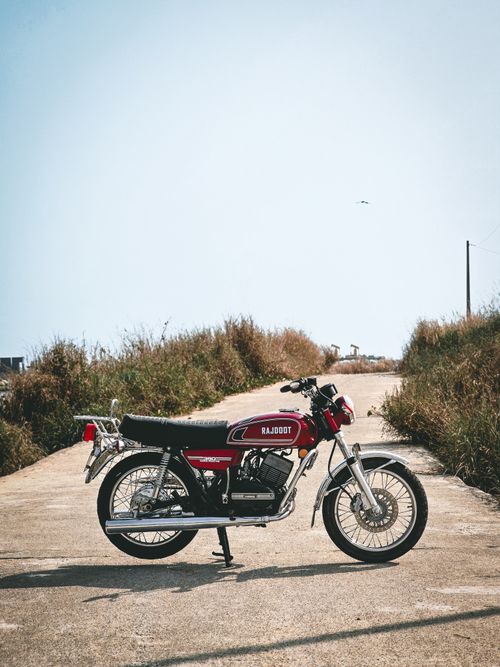 Free Vintage Rajdoot motorcycle parked outdoors on a winding country road in Chirayinkeezhu, India, under a clear blue sky. Stock Photo
