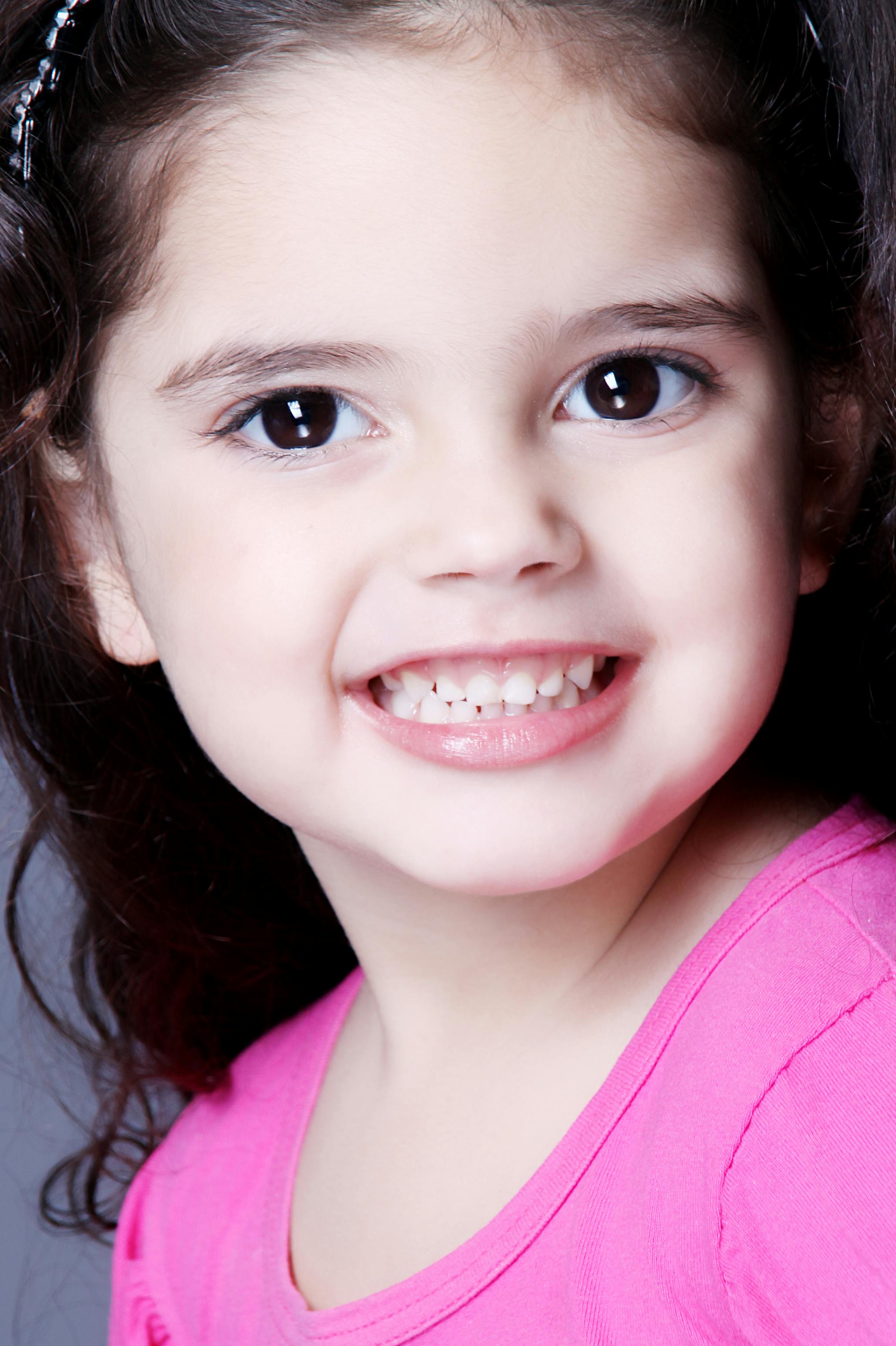 Close-up portrait of a young girl smiling happily in a pink shirt.