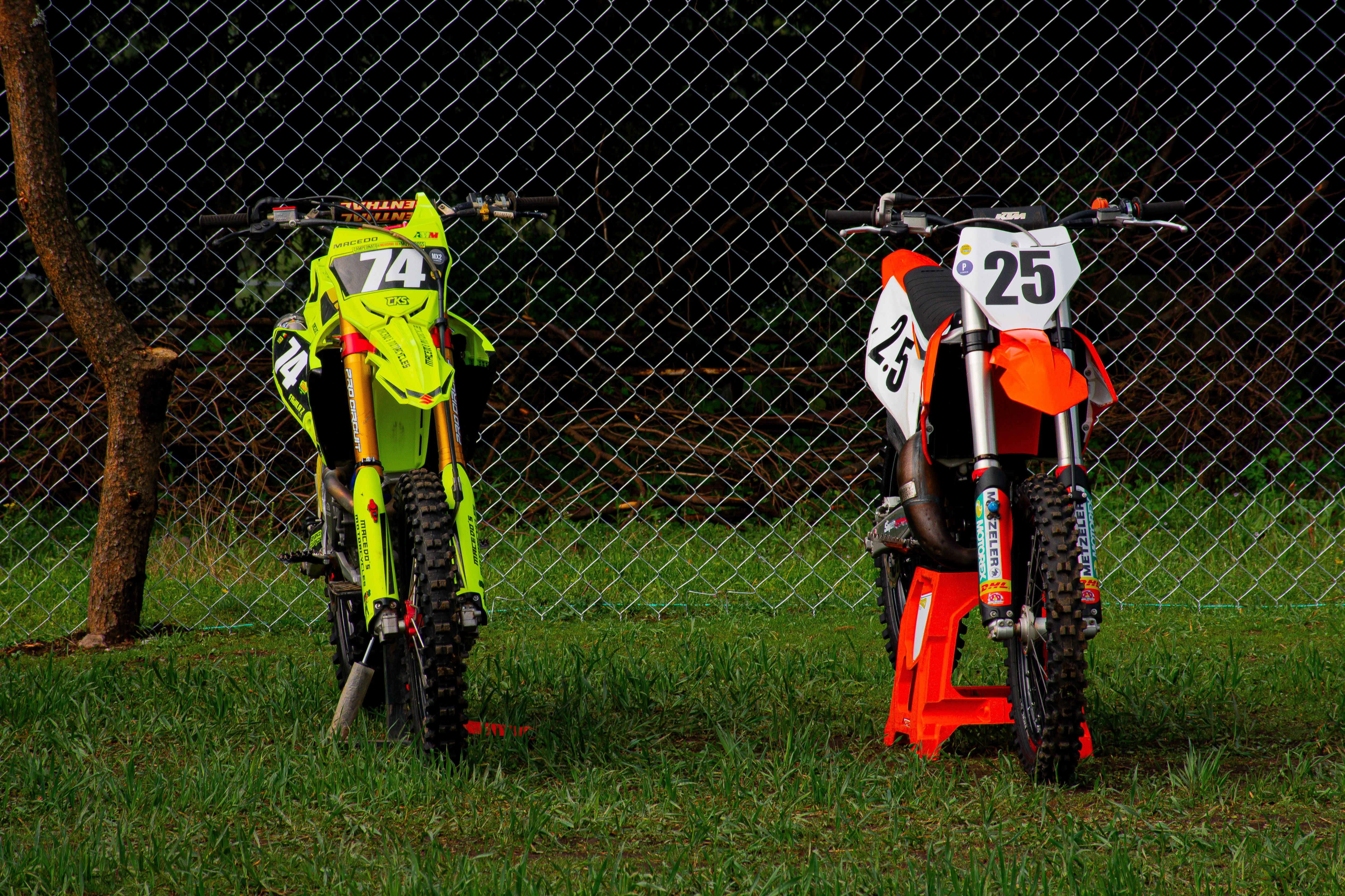 Two vibrant dirt bikes parked beside a fence in Mexico City, perfect for motocross enthusiasts.