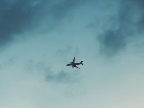 Silhouette of an airplane soaring through a cloudy blue sky, creating a serene travel mood.