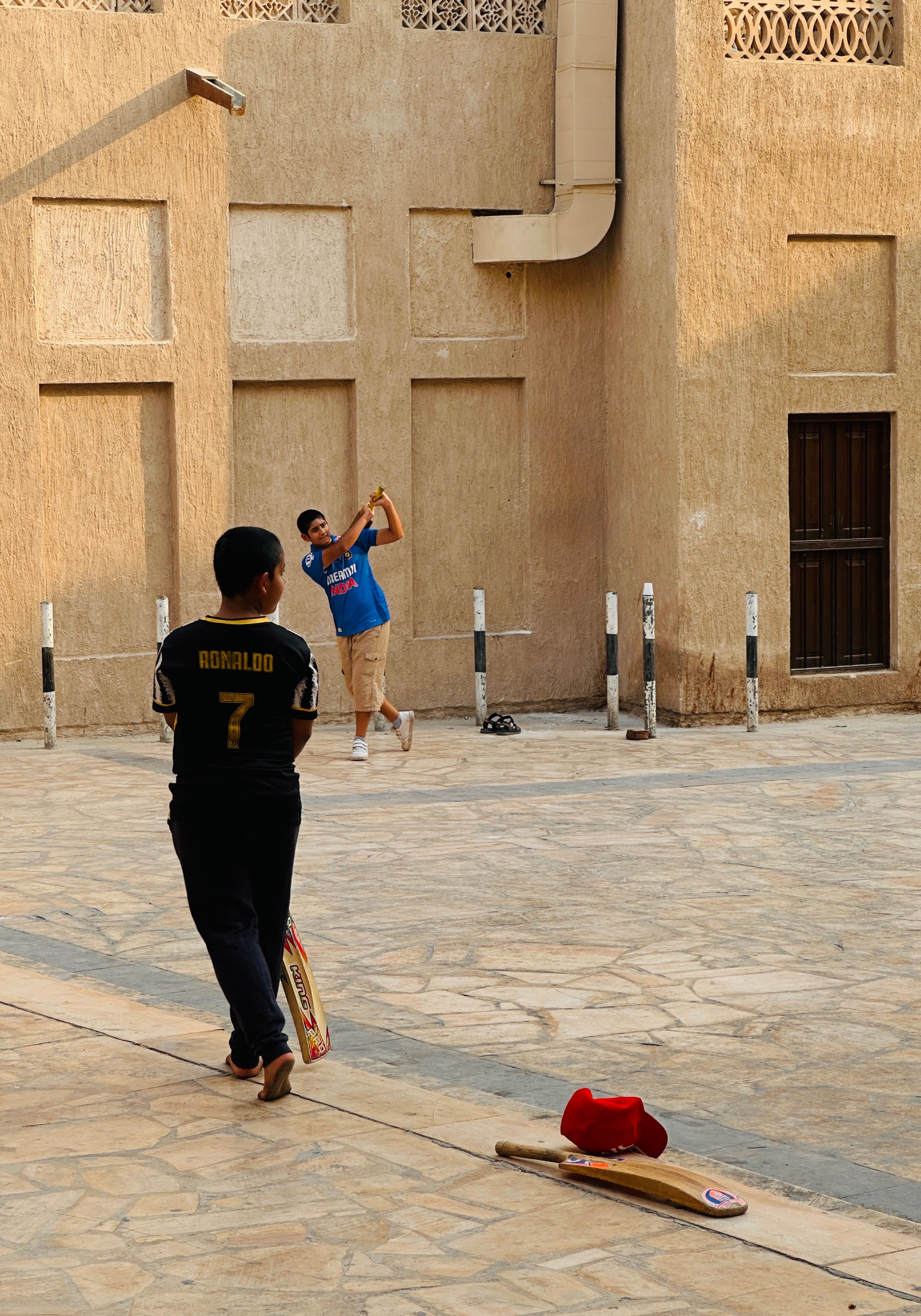 Casual street cricket game with two players in an urban setting during daylight.