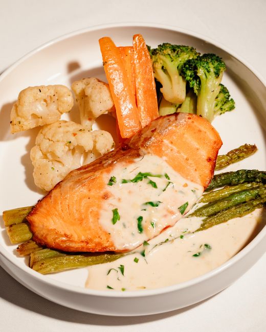 Two flaky salmon fillets with charred lemon slices sitting in an air fryer basket next to a pile of bright green roasted asparagus spears.