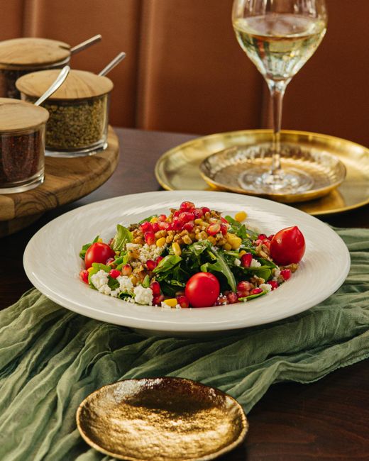 A mason jar of red wine vinaigrette with visible flecks of Dijon mustard and garlic, being poured over a bed of mixed greens.