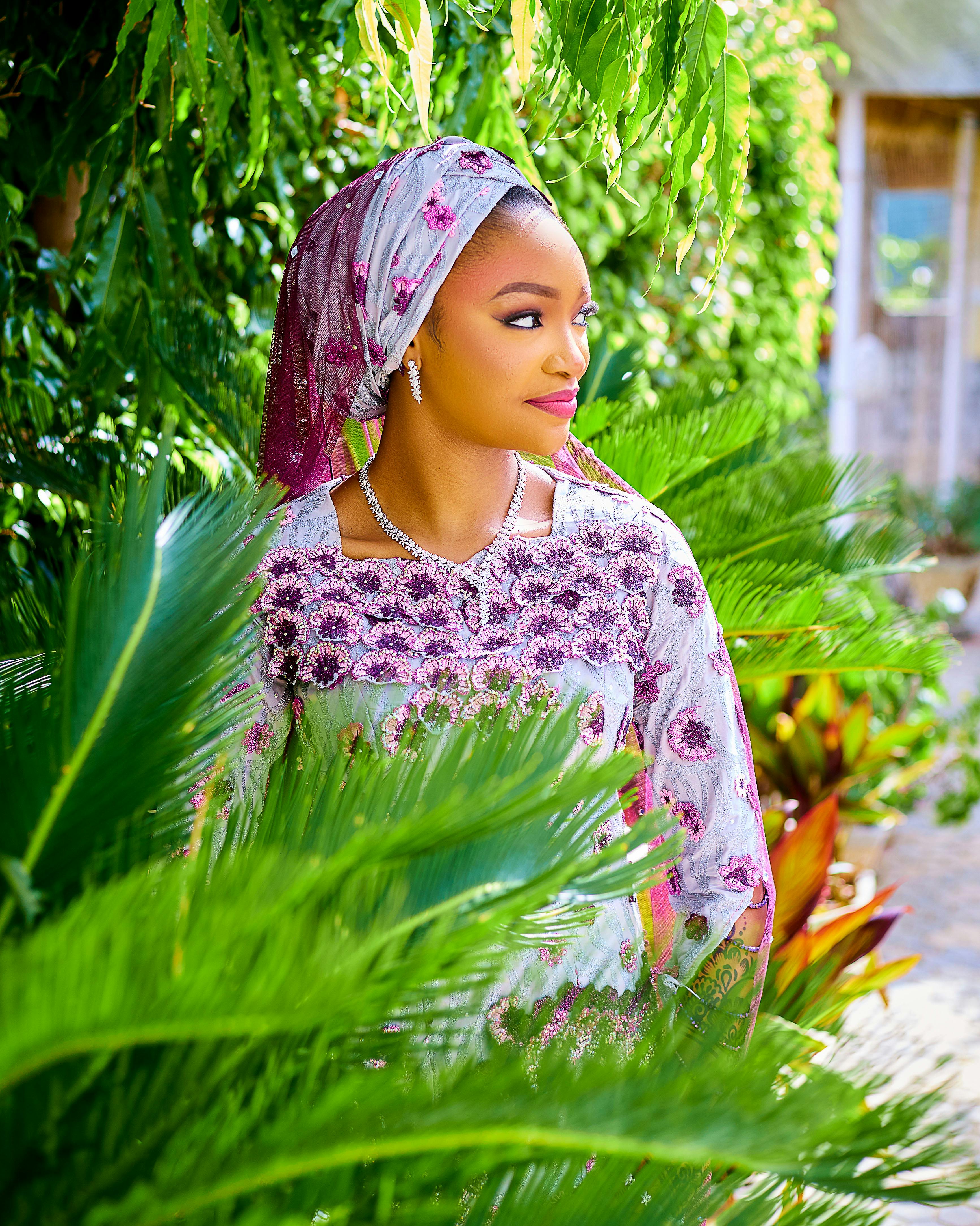 A beautiful woman in floral attire enjoys a sunny day surrounded by lush greenery.